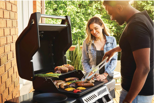 Napoleon Freestyle 365 propane grill on backyard patio with lid open, food grilling, and side shelves extended and happy couple grilling