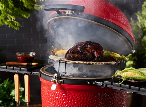 Classic Joe III ceramic grill open with roast and corn on cooking grates using Divide and Conquer system.With premium cart, 3-tier flexible cooking system, SlōRoller insert, and complete accessory set for ultimate outdoor grilling versatility.