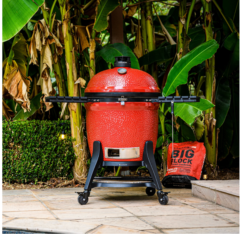 Big Joe III 24-inch ceramic grill with powder-coated steel cart on a porch setup, folding aluminum side shelves extended and charcoal in background