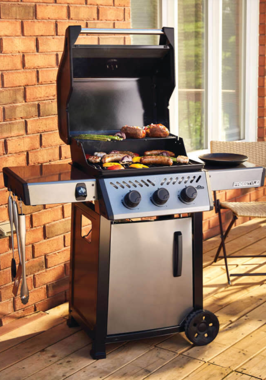 Freestyle 365 gas grill open with burgers, sausages and vegetables cooking on cast iron porcelain-coated cooking grids, flames visible under grates